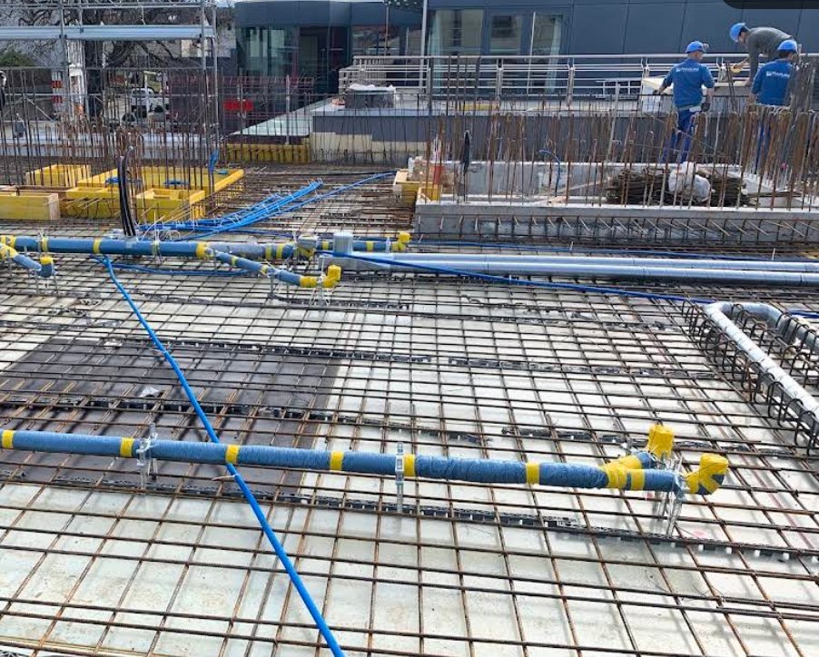 Chantier neuf : conduites d'eau bleues posées et fixées dans le ferraillage d'une dalle, avant le coulage du béton.