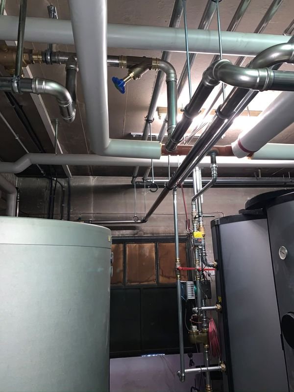 Local technique : deux ballons, réseau de conduites au plafond, pompe de circulation et vannes, conduites en inox serties.