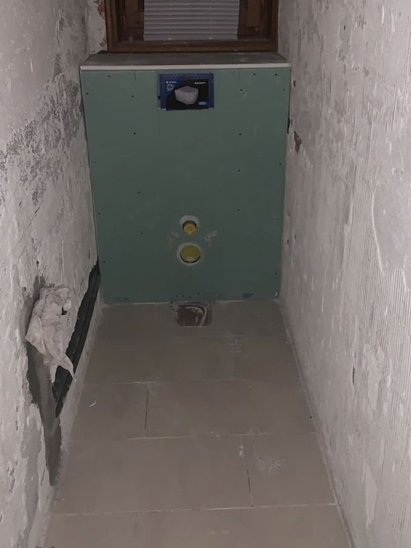 WC en rénovation : bâti-support Geberit habillé de plaques hydrofuges vertes, plaque de protection en place, raccords d'eau et d'évacuation en attente.