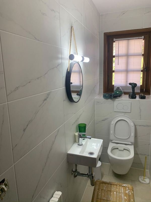 WC terminé : WC suspendu, plaque de commande Geberit, lave-mains avec mitigeur, carrelage blanc effet marbre.